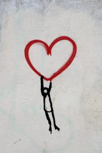 a stick figure holding on to a heart above its head
