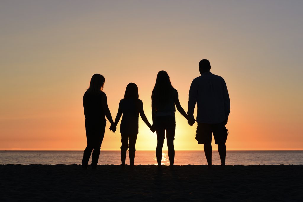 family on beach holding hands watching sunset