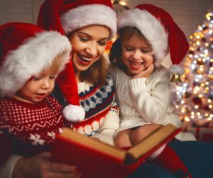 Mother with son and daughter (wearing Santa hats) on lap reading a Christmas story.