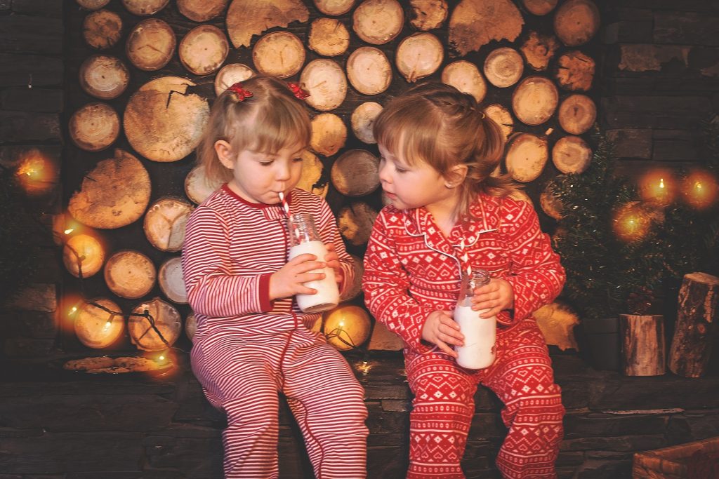 Two little girls dressed in Christmas pajamas drinking milk.