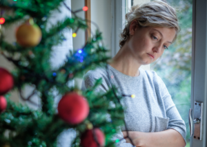 Depressed woman standing next to Christmas tree.